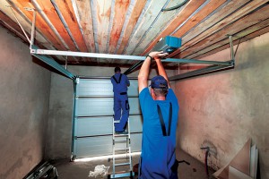 two workers installing motor mechanism for automatic garage door interior