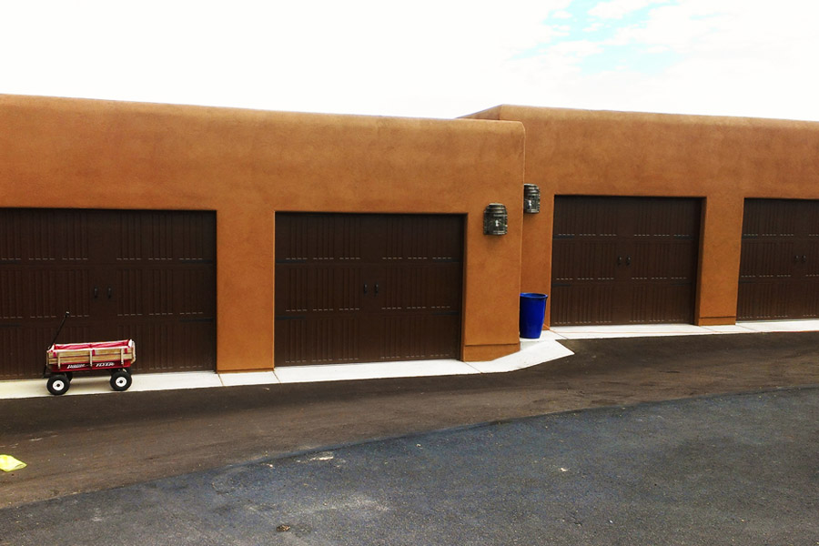 four dark stained wooden garage doors on stucco buildings